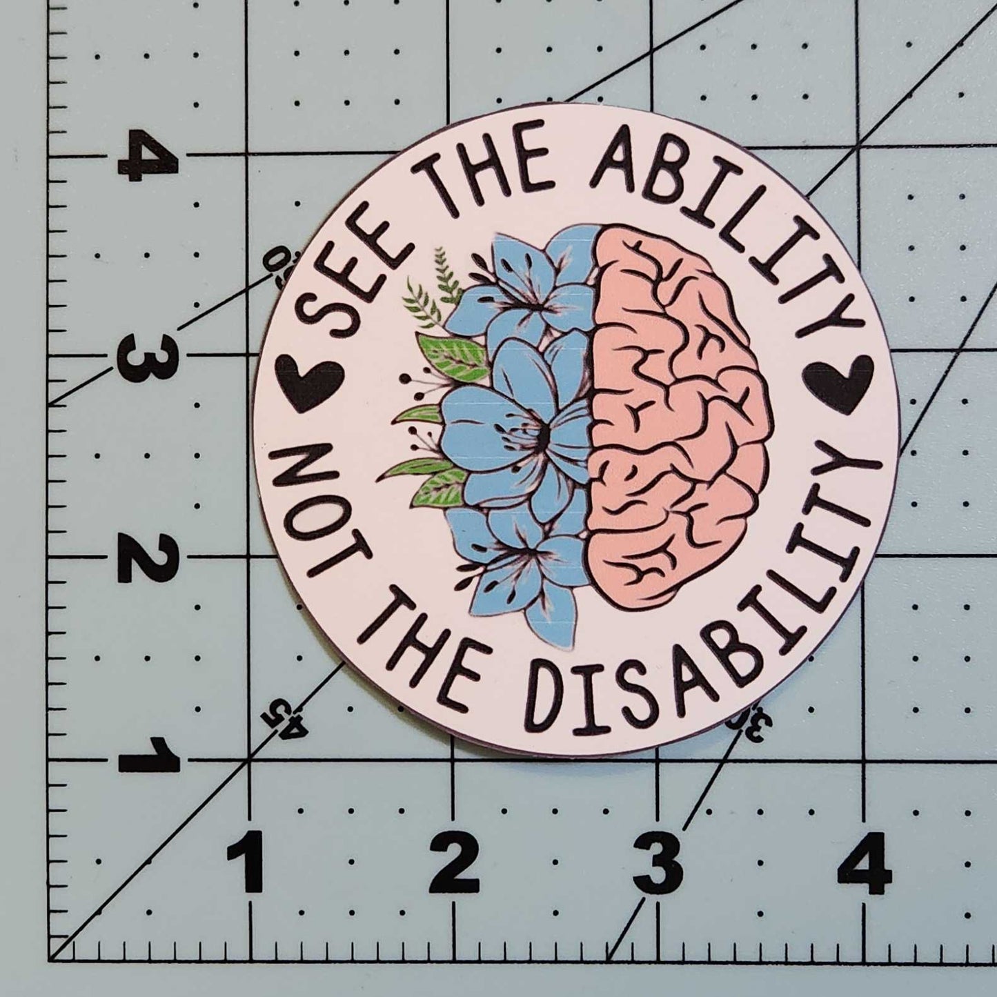 Circular sticker with brain and flower design on a cutting mat with ruler
