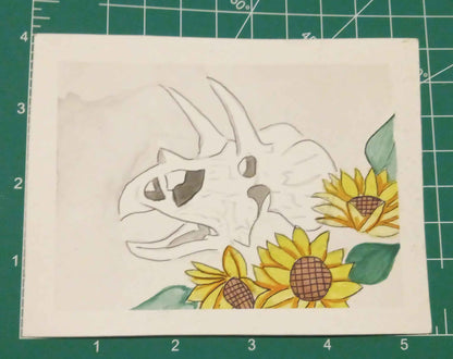 Card with a dinosaur and sunflowers design on a green cutting mat.