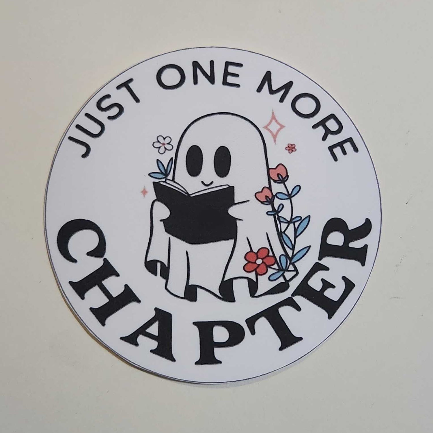 Circular sticker with a ghost design and text 'Just One More Chapter' on a white background